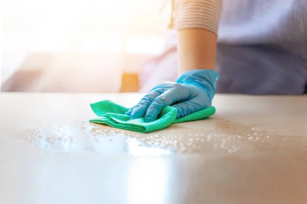 Woman in protective gloves wiping dust using a spray and a duster while cleaning her house.