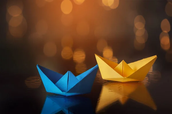 Yellow and Blue paper ship ships on dark background.