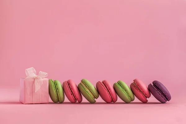Pink present and Row of french colorful macaroons, lying on pink background . — стоковое фото