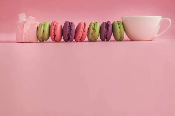 Розовый подарок и рожь французских цветных макарон и чашка кофе, лежащие на розовом фоне — стоковое фото