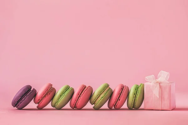 Pink present and Row of french colorful macaroons , lying on pink background.