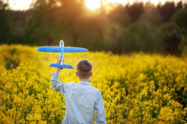 Sevimli Boy yaz gününde gün batımında elinde oyuncak uçak tutar. Geri görünüm.