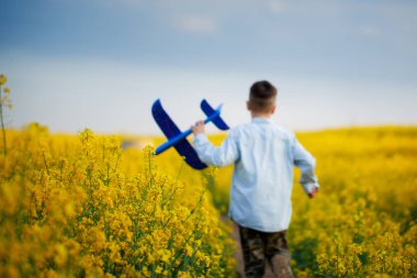 Güneşli bir yaz gününde sarı alanda yürüyen sevimli çocuk. Çocuk kağıt uçak başlatır. Bulanıklık ve yumuşak odaklama.