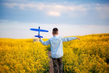Güneşli bir yaz gününde sarı alanda yürüyen sevimli çocuk. Çocuk kağıt uçak başlatır. Geri görünüm