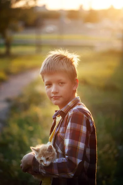 Niño feliz con un gatito en sus manos en la naturaleza en verano . — Foto de Stock