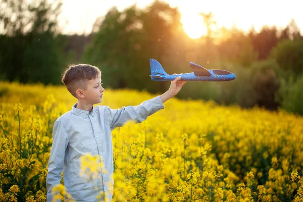 Kluk hraje s hračkářském letadlem v zapadajícím slunci a sní o cestě v letním dni. — Stock fotografie