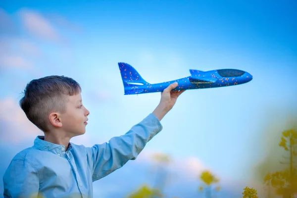 Schattige jongen speelt met een speelgoed vliegtuig in de blauwe lucht en droomt van reizen. Hand met blauwe speelgoed vliegtuig. — Stockfoto