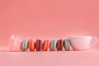 Pembe mevcut ve Fransız renkli macaroons ve kahve fincan Satır, mercan arka plan üzerinde yalan