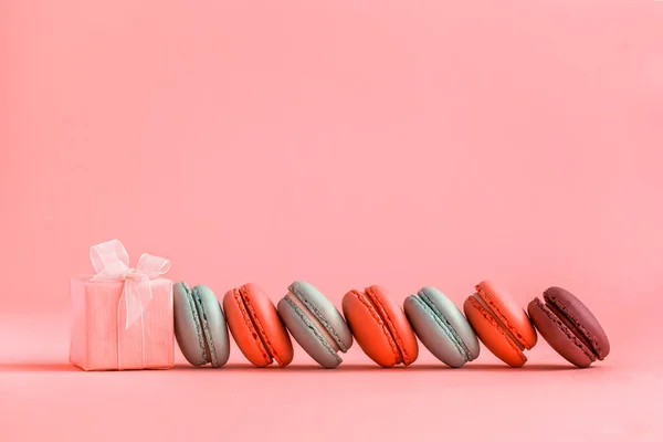 Розовый подарок и ряд французских красочных макарон, лежащих на коралловом фоне . — стоковое фото