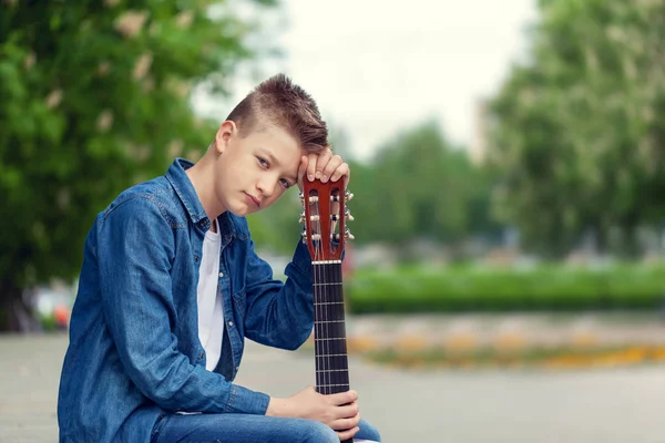 Porträt Teenager Junge mit Gitarre sitzt im Park. — Stockfoto