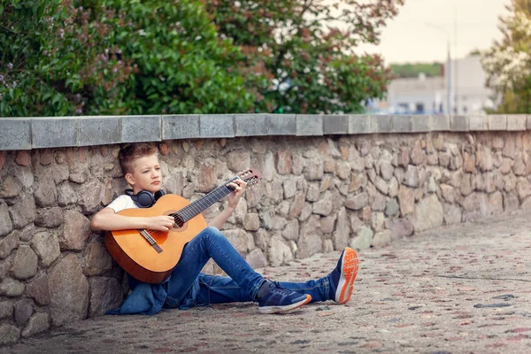 Teenager mit Akustikgitarre und Kopfhörer im Park. — Stockfoto