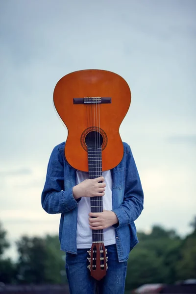 Adolescente con una guitarra en lugar de una cabeza en el parque. Joven loco y fresco con una guitarra . —  Fotos de Stock