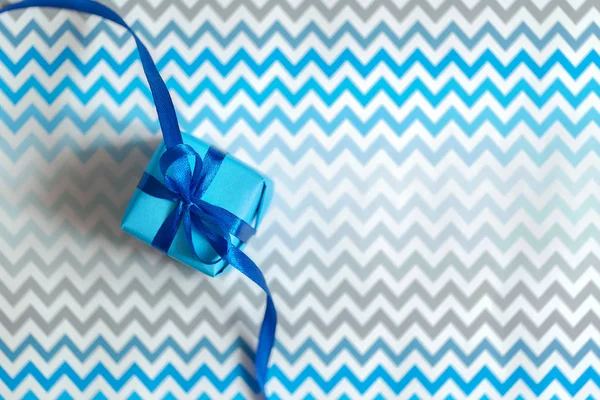 Одна синя подарункова коробка і пов'язана з синім бантом на стрічковому зигзагоподібному фоні . — стокове фото