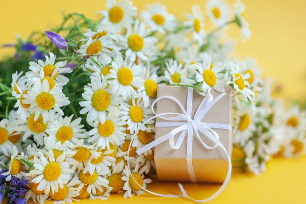 Chamomile flowers and gift or present box on yellow background. Holiday celebration concept. — Stock Photo, Image