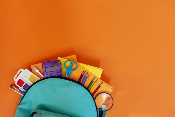 Full turquoise School Backpack with different supplies on orange background. FLat lay. Concept back to school. — Stock Photo, Image