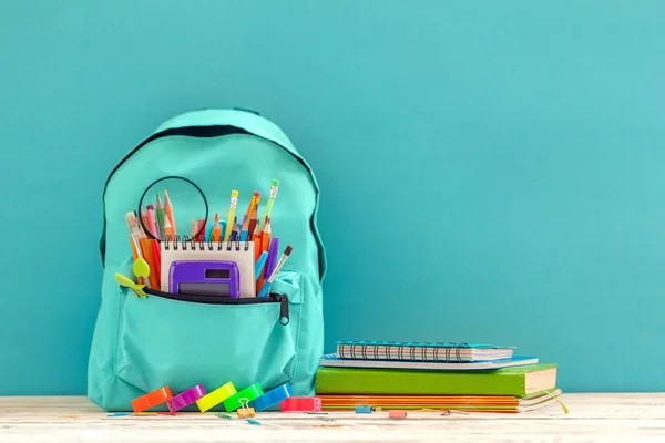 Voller blauer Schulrucksack mit verschiedenen Vorräten auf blauem Hintergrund. Konzept zurück zur Schule — Stockfoto