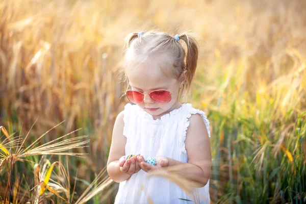 Küçük kız güneşli yaz alanında oynuyor. Beyaz elbise ve güneş gözlüğü bebek. — Stok fotoğraf