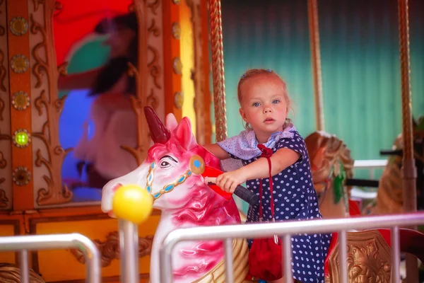 Adorable niña n vestido de lunares montar en un caballo carrusel alegre ir al aire libre  . — Foto de Stock