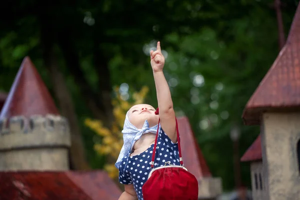 ハンカチと水玉模様の小さな女の子が公園を歩いている。笑顔の女の子が見上げて親指を見せる. — ストック写真