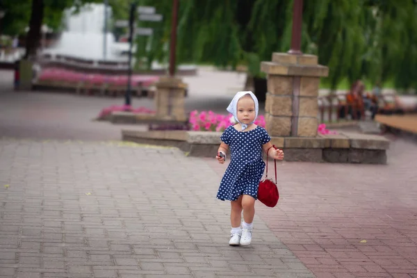 Mała dziewczynka w chusteczkę i Polka-dot sukienka spaceru po parku w lecie. — Zdjęcie stockowe