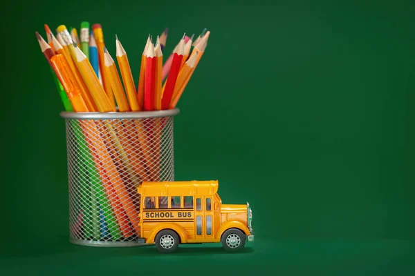 Education and back to school concept. Yellow retro school bus and pencils in basket on dark green background.