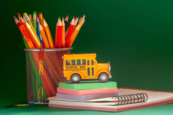 Education and back to school concept. Yellow retro school bus and pencils in basket, textbooks on dark green background