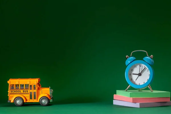 学校の概念に戻る 濃い緑色の背景に黄色のスクールバスと青い目覚まし時計 — ストック写真