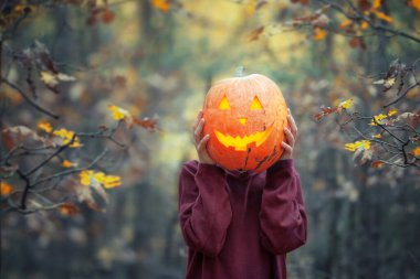 Karanlık sonbahar ormanlarında kafasının önünde oyulmuş balkabağı tutan çocuk..