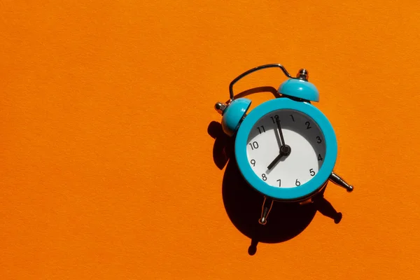 Blue alarm clock on orange background. Back to school concept. Creative design, minimal concept. Wake up Morning.