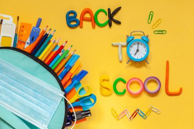 Okul konseptine geri dönelim. Sarı arka planda farklı malzemelerle dolu mavi okul çantası. FLat yatıyordu.