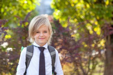 Sırt çantalı sevimli sarışın çocuk okula gidiyor. Gülümseyen öğrenci git ilkokula çalış. Okul konseptine dönelim.