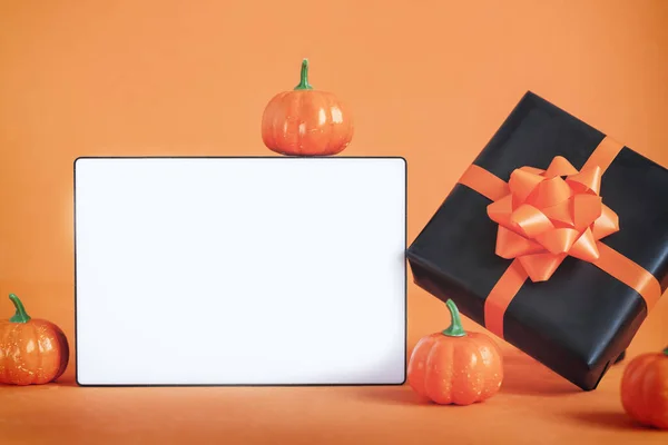 Black present or gift box with orange ribbon and pumpkin and empty blank lightbox on orange background. Happy halloween