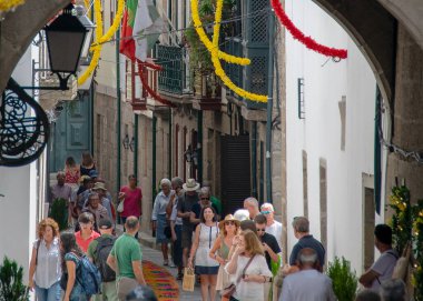 Guimaraes, Portekiz: 14 Ağustos 2023: Portekiz 'in Guimaraes şehrinde insanlarla dolu ve çelenklerle dolu bir caddeyi çerçeveleyen taştan kemer yoluyla çekilen ön manzara fotoğrafı. 