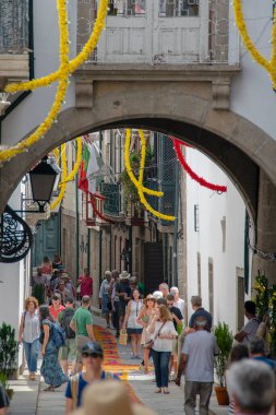 Guimaraes, Portekiz: 14 Ağustos 2023: Portekiz 'in Guimaraes şehrinde insanlarla dolu ve çelenklerle dolu bir caddeyi çerçeveleyen taştan kemer yoluyla çekilen ön manzara fotoğrafı. 