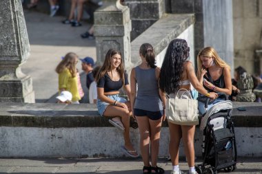 Braga, Portekiz: 14 Ağustos 2023: Portekiz 'in Bom Jesus do Monte Braga kentinde tarihi bir taş duvarın yanında oturan ve konuşan genç kadınlar