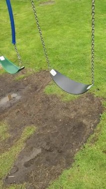 Şehir parkında yavaşça hareket eden boş bir salıncağın yavaş çekim dikey videosu