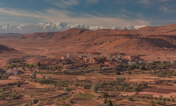 Ouarzazate, Morocco, Africa - January 15, 2014: Panoramic view of a small village surrounded by crops and the mountain range of snowy mountains Atlas in the background, Sahara, Morocco