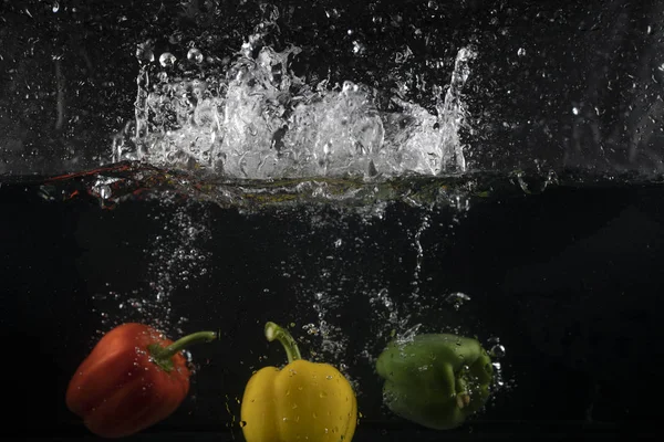 stock image several coloured paprika falling into water splash with many bubble