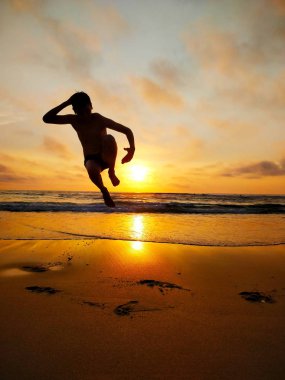 Jumping teen at sunset on the beach clipart