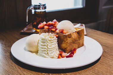 Ballı tost çilekli tost, beyaz bir tabakta dondurma sütü, ahşap bir masada.