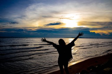Deniz kenarındaki bir kayanın üzerinde elleri havada bir kız. Özgürlük ve barış. İçim rahat olsun. Deniz meltemi, batan güneş.