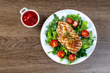 Ahşap bir masada, beyaz tabakta domatesli ızgara tavuk göğsü. Sağlıklı yemek.