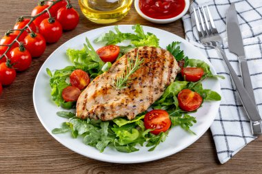 Ahşap bir masada, beyaz tabakta domatesli ızgara tavuk göğsü. Sağlıklı yemek.