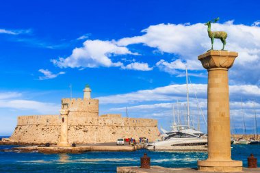 Greece travel, Dodecanese. Rhodes island. entrance of Mandraki Harbor with symbol statue of deer and old lighhouse clipart