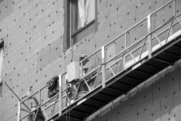 Trabajadores de la construcción con sombreros duros trabajan en la fachada — Foto de Stock