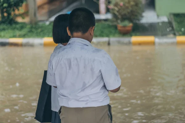 男孩和女孩等待在大雨横穿被淹没的街道在重的暴雨之前回家放学后 — 图库照片