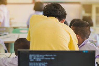 Sarı gömlekli sınıf, kontrol ve yardımcı erkek öğretmen öğrencilerin bilgisayar sınıfta çalışır.