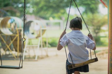 Genç kızın arkadan görünüm oturup bekle salıncaklar onun arkadaşı parkta.