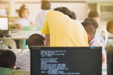 Sarı gömlekli sınıf, kontrol ve yardımcı erkek öğretmen öğrencilerin bilgisayar sınıfta çalışır.