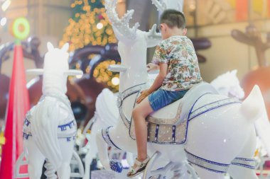 Çok güzel Asyalı küçük çocuk çocuk üstünde yuvarlak atlıkarınca Ren geyiği Noel lunapark, neşeli bir gitmek sürme.